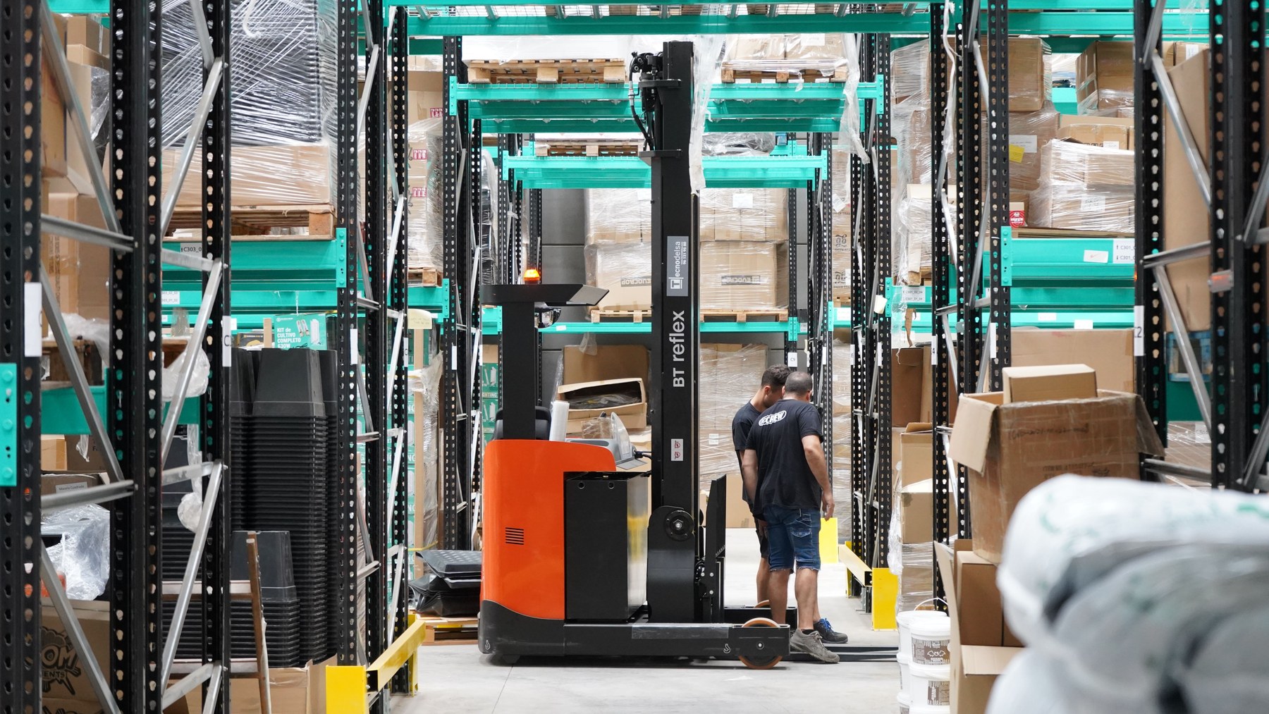 Two warehouse employees beside a reach truck and stored pallets